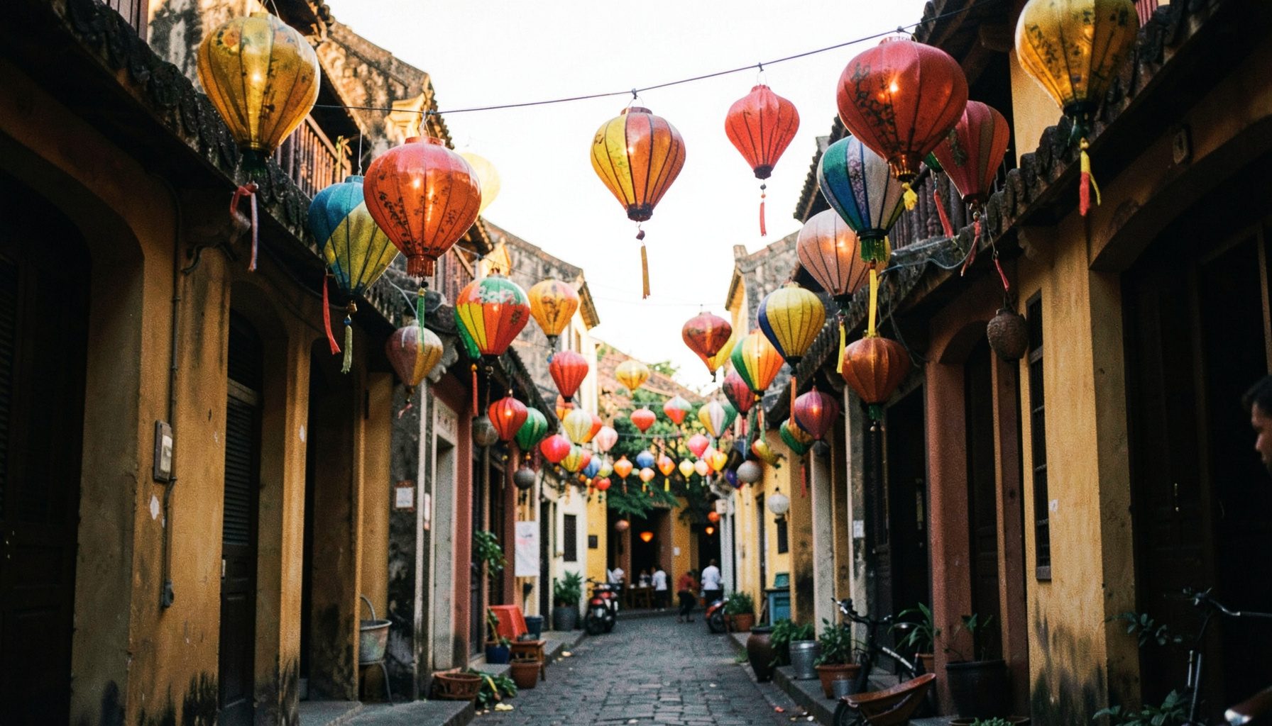 Colorful lanterns hanging above a narrow ancient street in Hoi An's old town, warm amber and red tones, late afternoon light