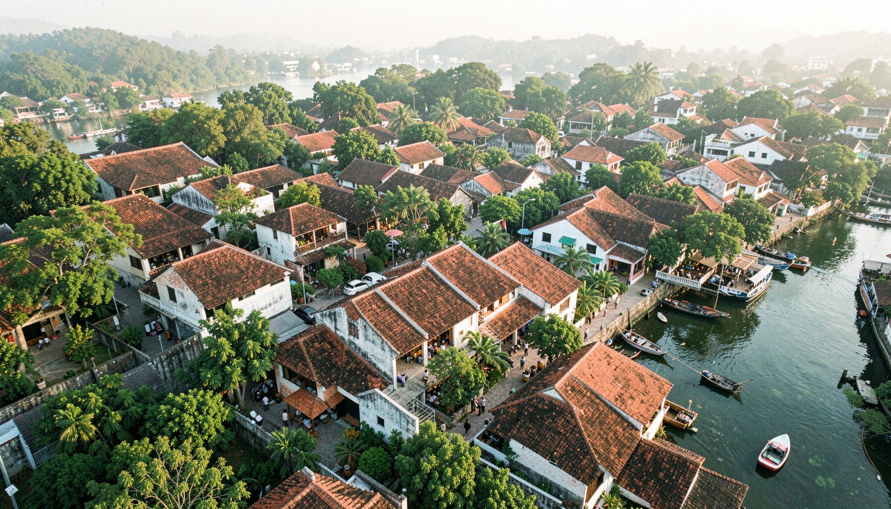 Aerial view of Hoi An's Cam Nam ward with riverside greenery, terracotta rooftops, and the hotel's neighborhood in soft morning light