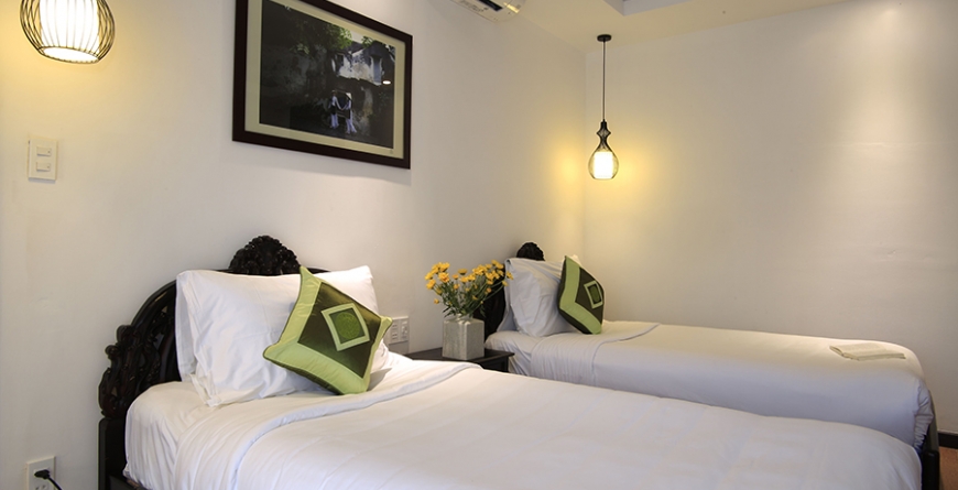 Twin bed room with white linens, green accent pillows, pendant lights, and framed photo on wall; neutral tones, simple elegance